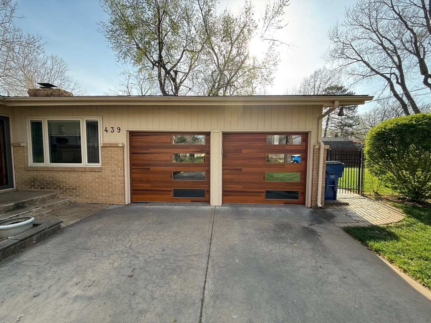 Pair of modern wood-look garage doors with glass windows on a brick home