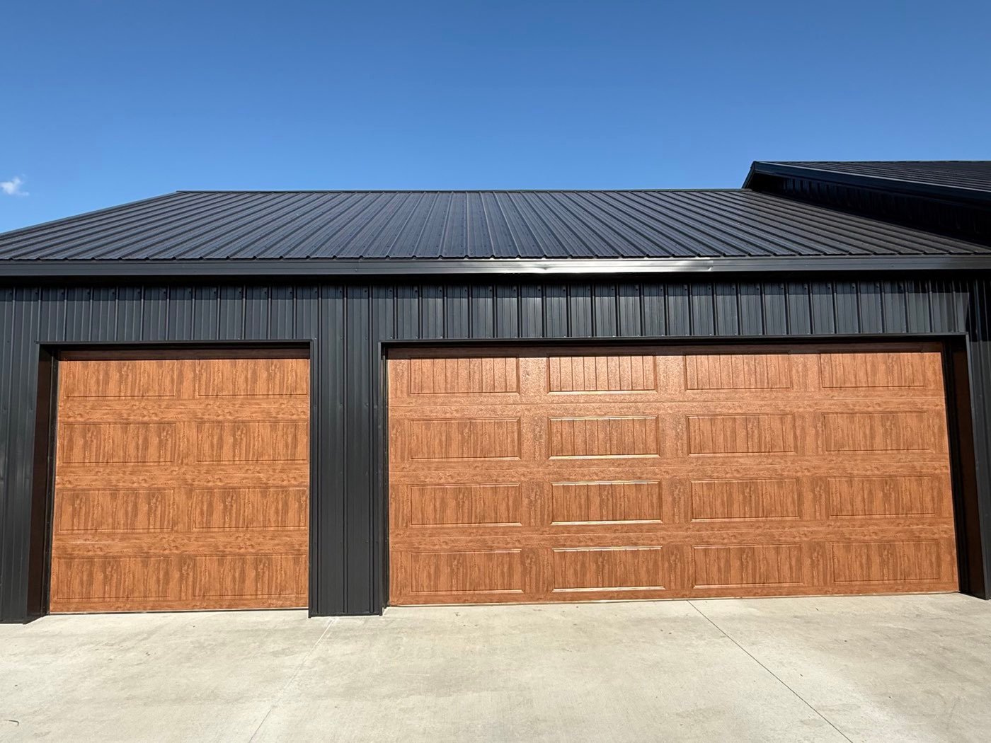 Two wood-grain garage doors on a black steel building